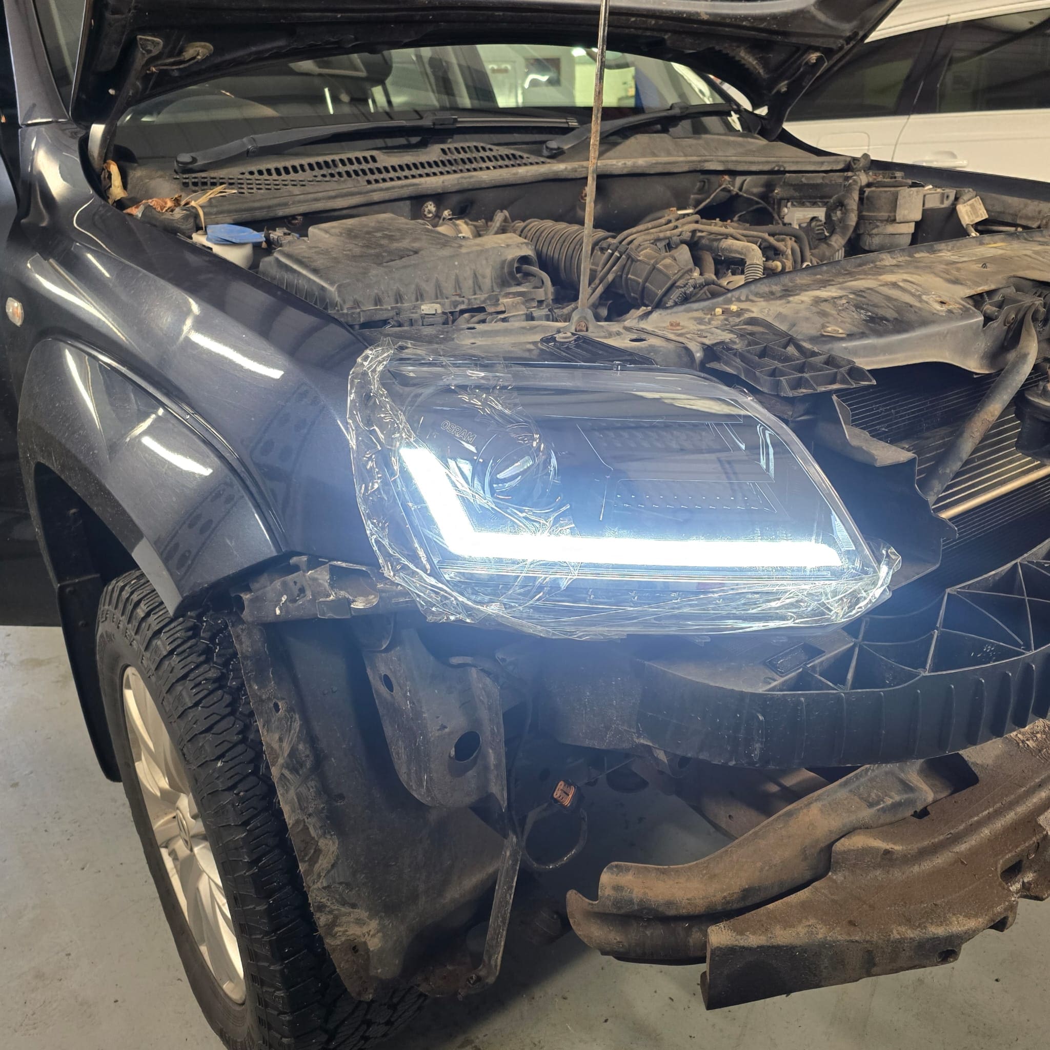Workshop photo showing VW Amarok during black OSRAM LED headlamp installation